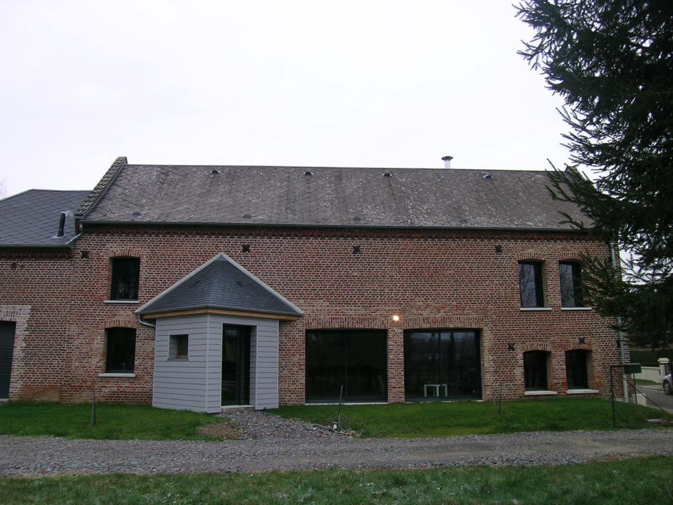 Bâtiment en briques au toit gris, petite structure en bois à l'avant, fenêtres et pelouse verte.
