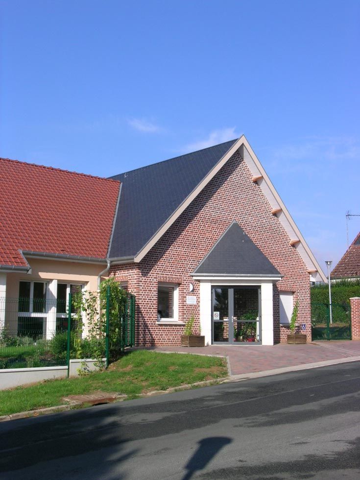 Un bâtiment en briques rouges avec un toit et une entrée gris foncé, par une journée ensoleillée.