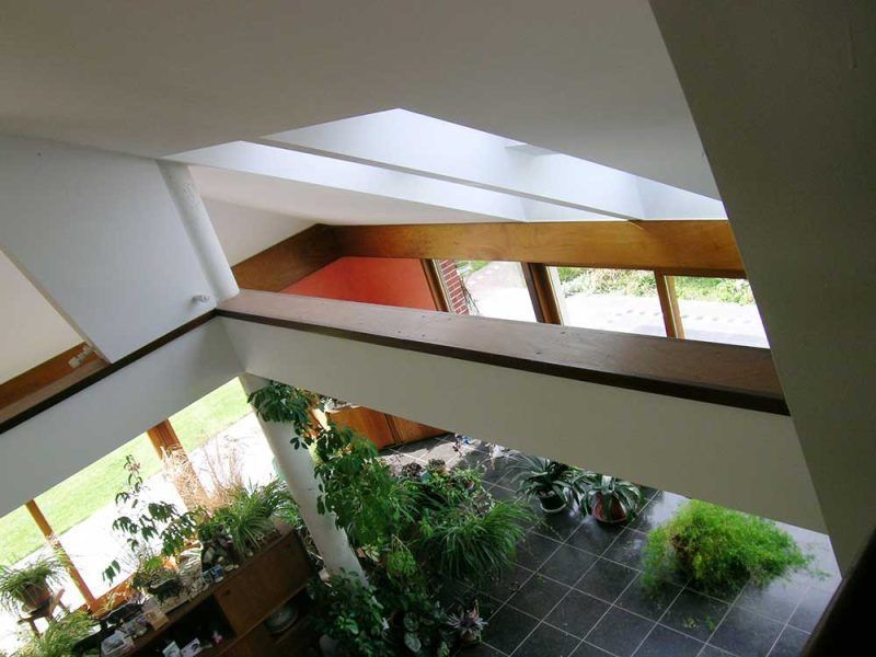 Vue intérieure d'un bâtiment moderne aux murs blancs géométriques, aux poutres en bois apparentes et à une fenêtre donnant sur la verdure.