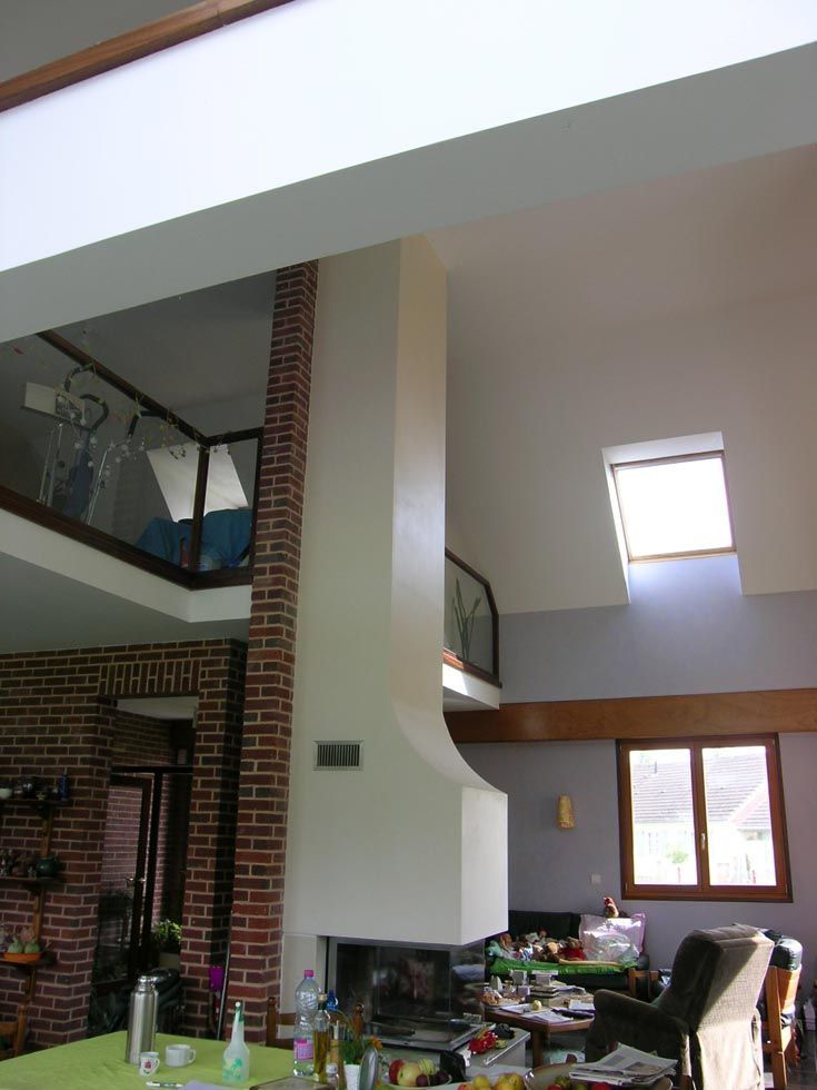 Vue intérieure d'une maison moderne avec cheminée, mezzanine et puits de lumière.