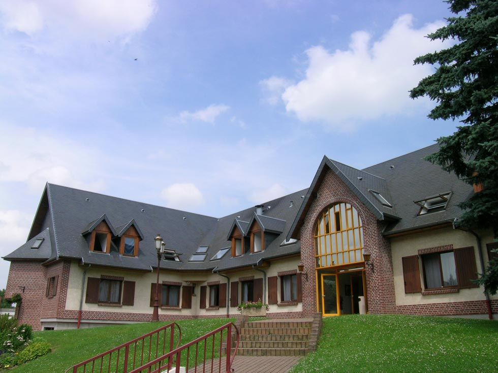Bâtiment en briques avec plusieurs pans de toit à pignons, des lucarnes et une pelouse.