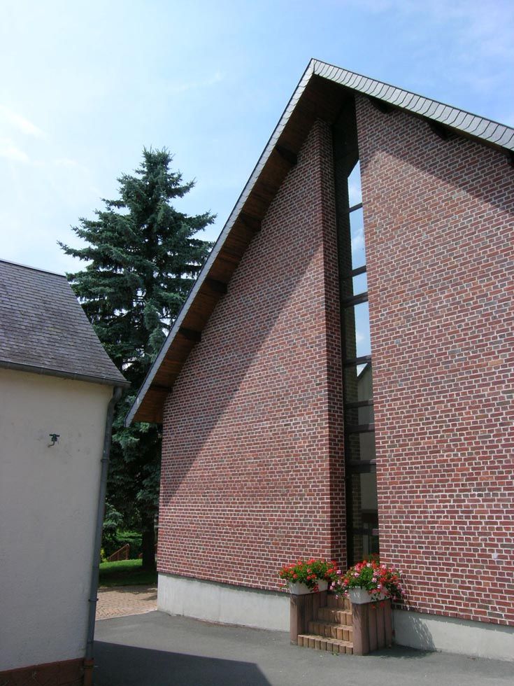 Bâtiment en briques avec toit en pente, haute fenêtre et jardinière, avec un arbre bleu en arrière-plan.