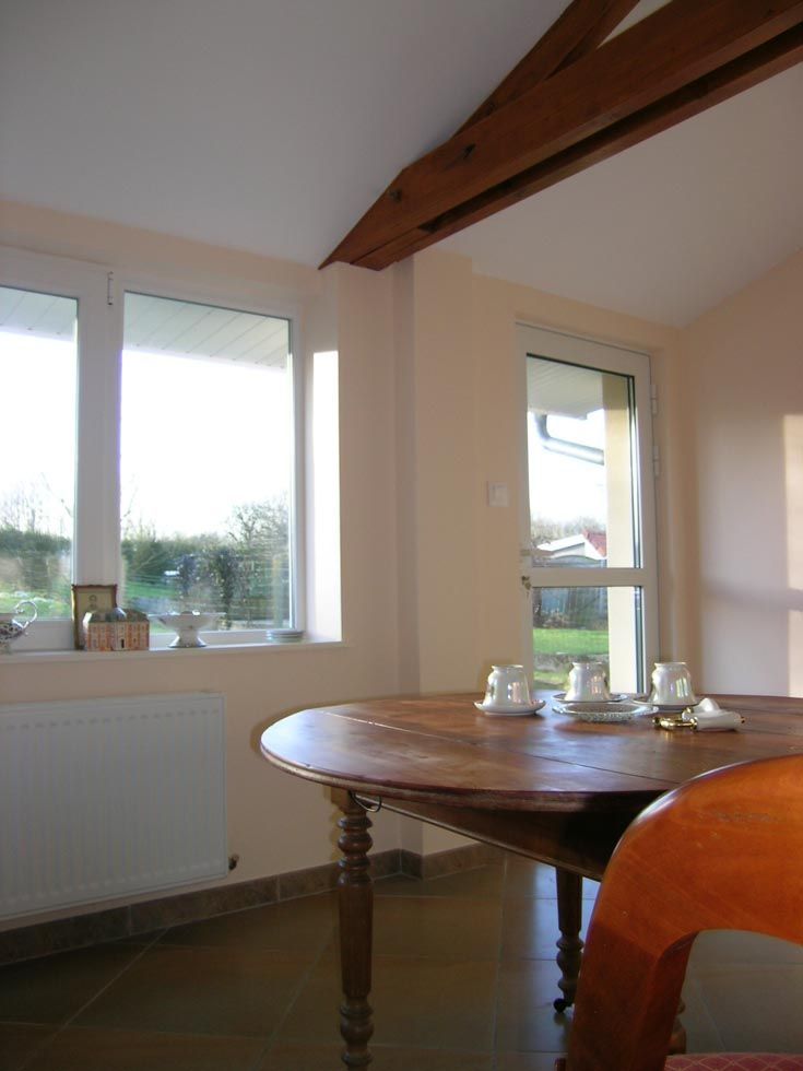 Salle à manger avec une table ronde en bois, des fenêtres et des poutres apparentes.