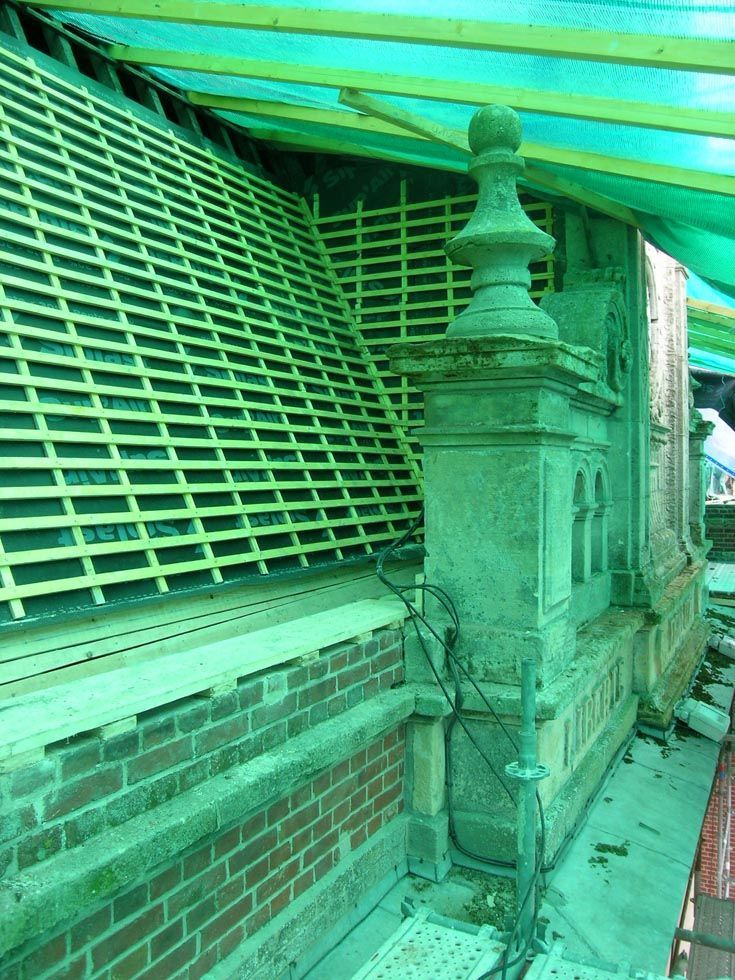 Extérieur du bâtiment en construction, toiture apparente et échafaudages. Bâche verte au-dessus.