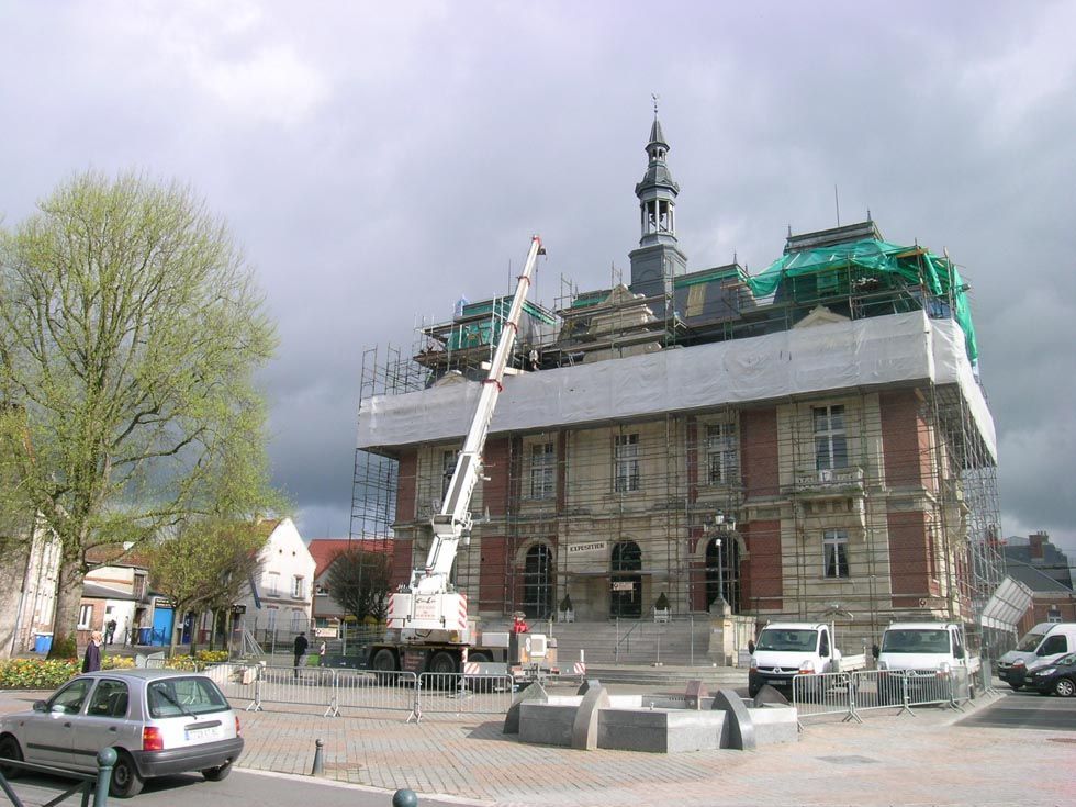 L'hôtel de ville est en rénovation, avec des échafaudages, une grue et des travaux de construction sur la place de la ville.