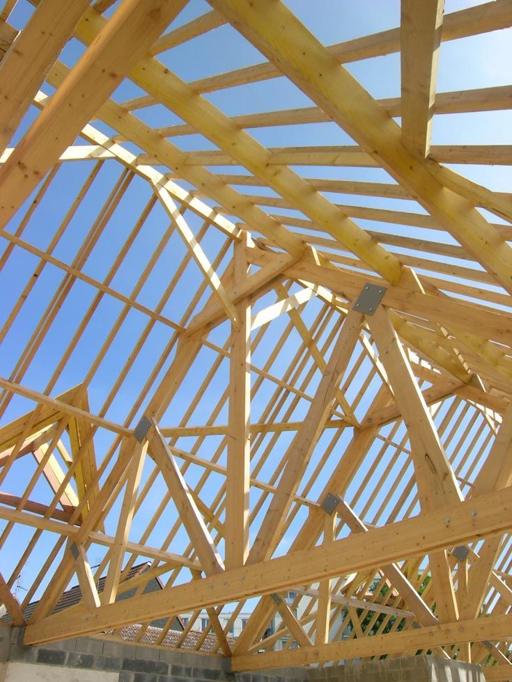 Charpente de toit en bois en construction, sur fond de ciel bleu.