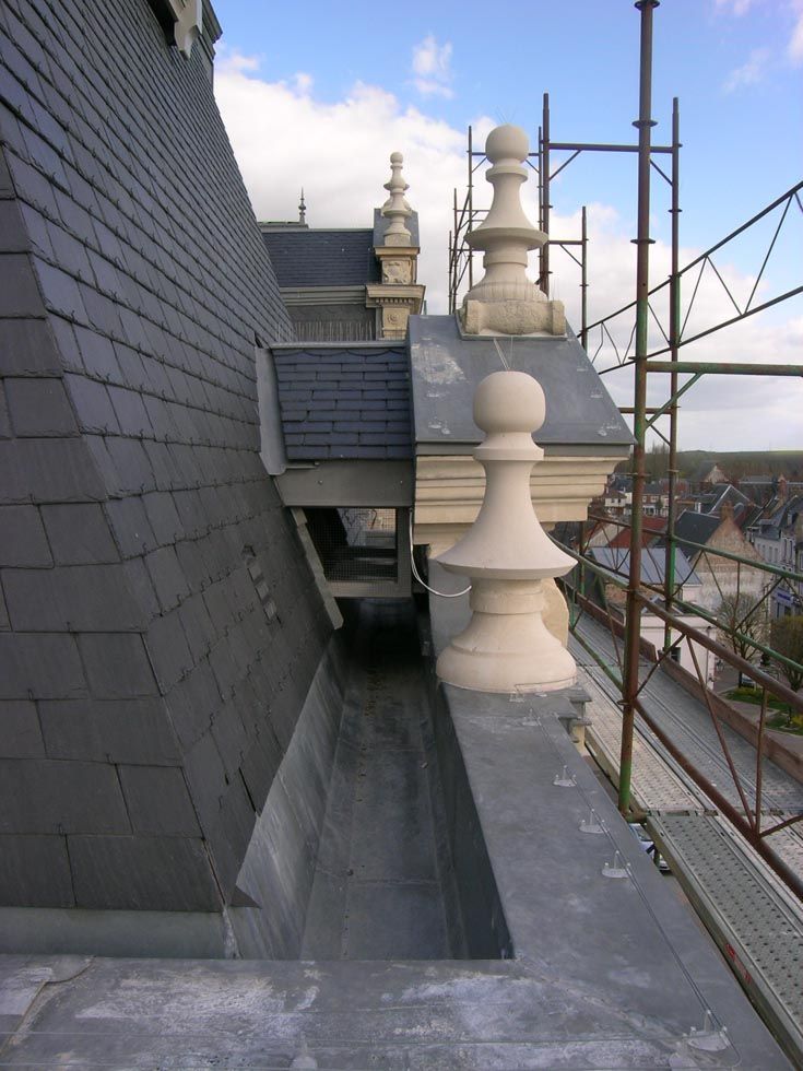 Toit en ardoise avec gouttière, éléments ornementaux en pierre et échafaudages.