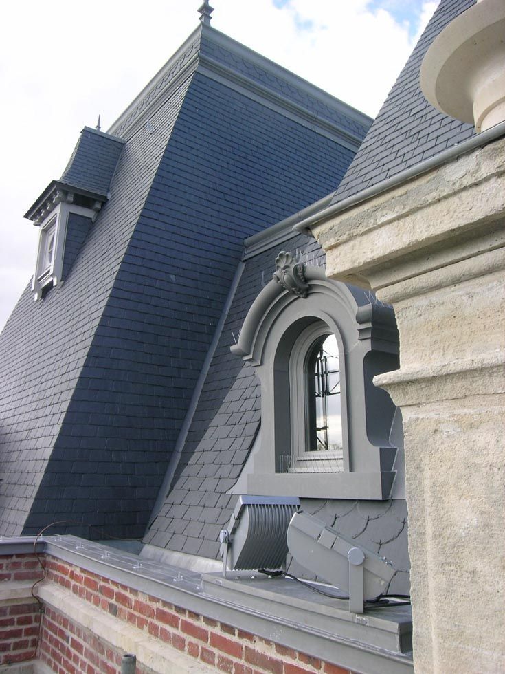 Détail architectural d'un toit en ardoise sombre avec une lucarne. Construction en brique et en pierre visible.