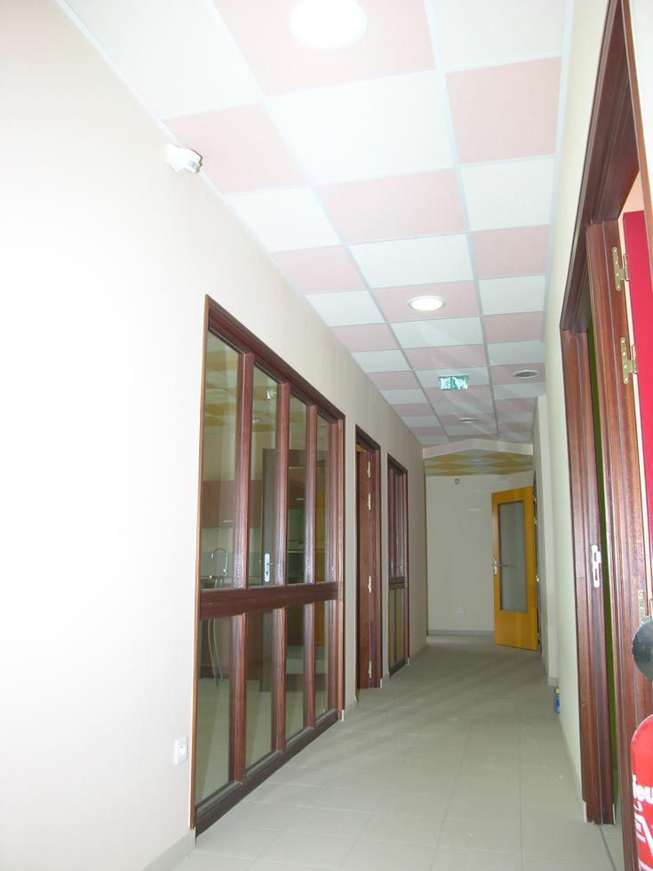 Couloir avec fenêtres vitrées, portes marron et plafond à damier rose et blanc.