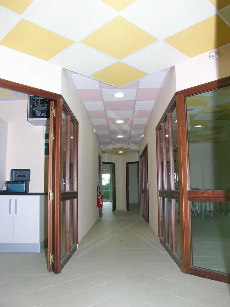 Couloir étroit avec portes vitrées et plafond à damier.