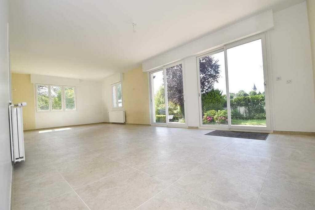 Salon vide avec de grandes fenêtres, un intérieur lumineux et un sol carrelé.