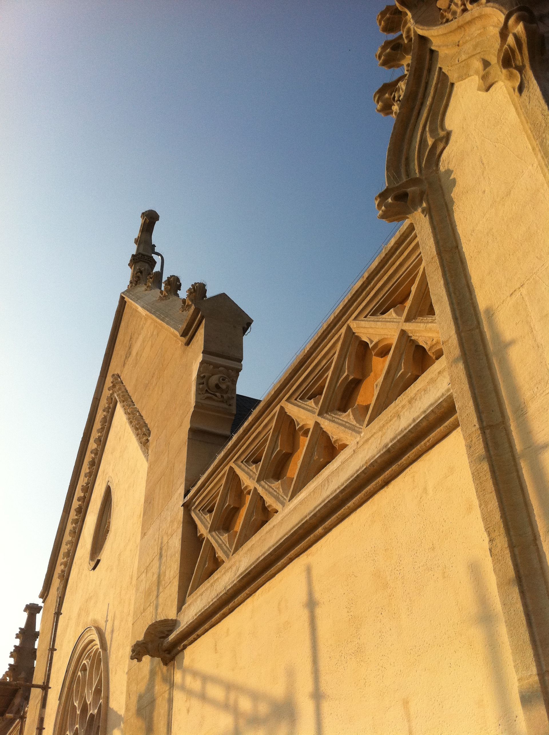 Détail architectural d'un bâtiment beige orné de motifs en losange et de bords sculptés, se détachant sur un ciel bleu.