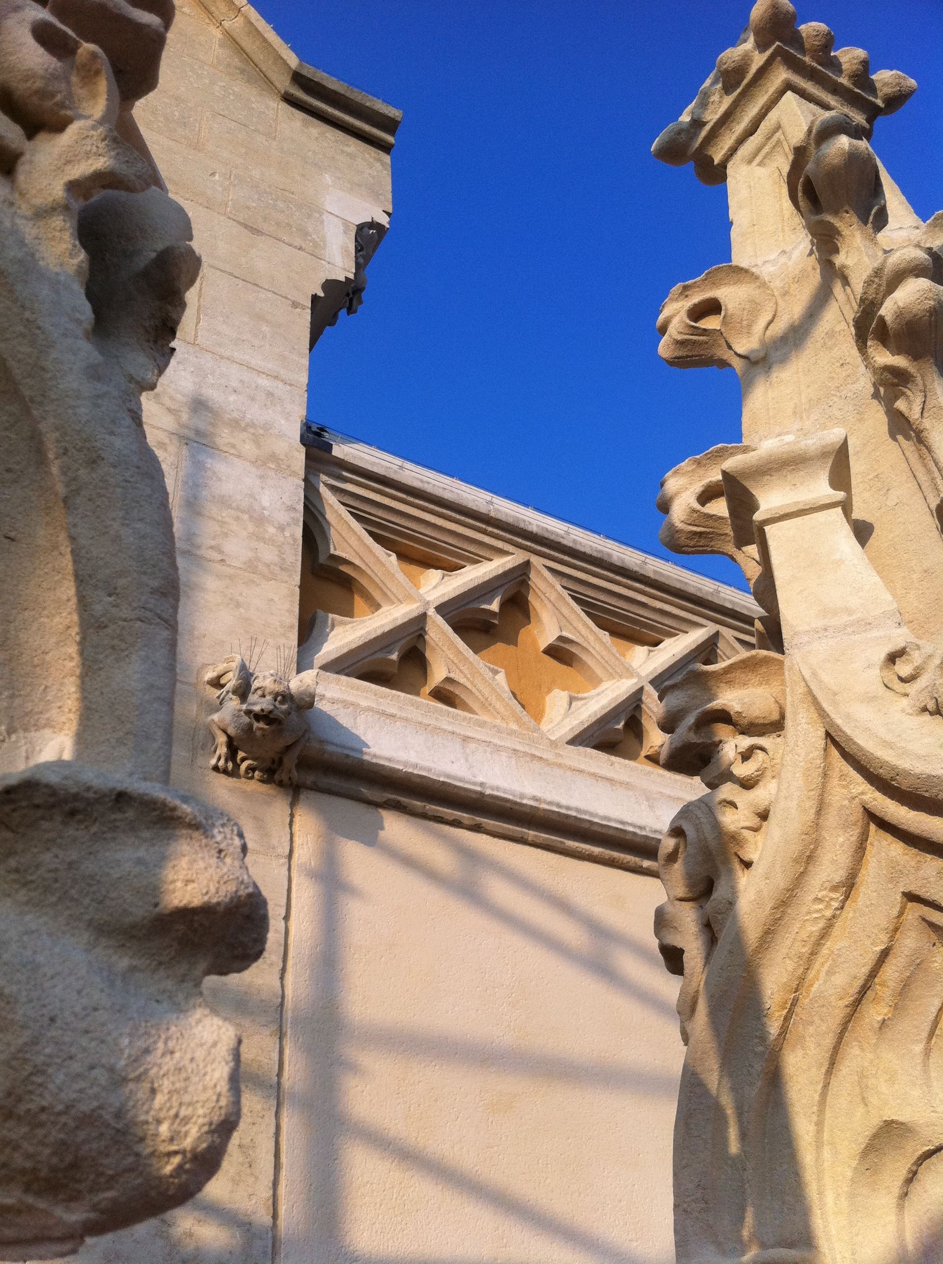 Façade d'un bâtiment en pierre ornée de gargouilles se détachant sur un ciel d'un bleu éclatant.