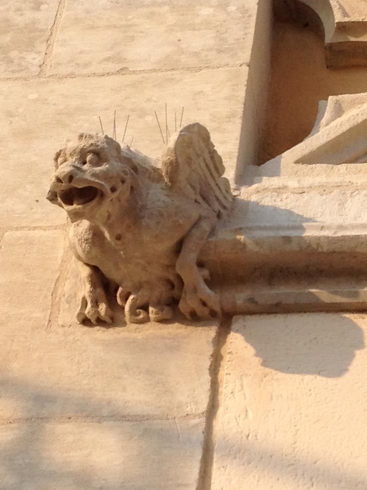 Gargouille en pierre ailée à la bouche ouverte, ornant la façade d'un bâtiment.
