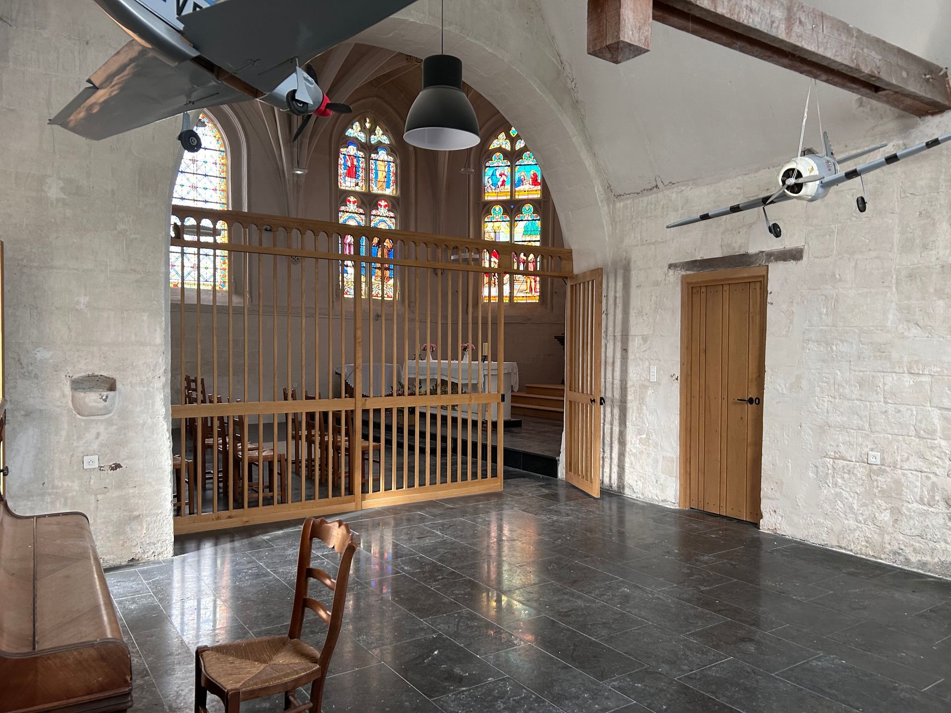 Intérieur d'une ancienne église avec murs en pierre, vitraux et bancs en bois.
