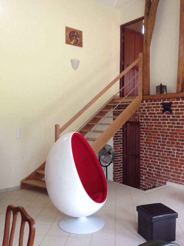 Fauteuil œuf moderne à intérieur rouge dans une pièce avec un escalier en bois et un mur de briques apparentes.