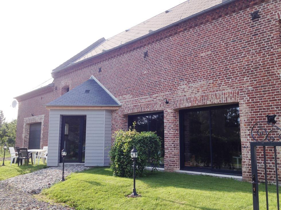 Bâtiment en briques avec une entrée grise, de grandes fenêtres noires et de l'herbe verte.