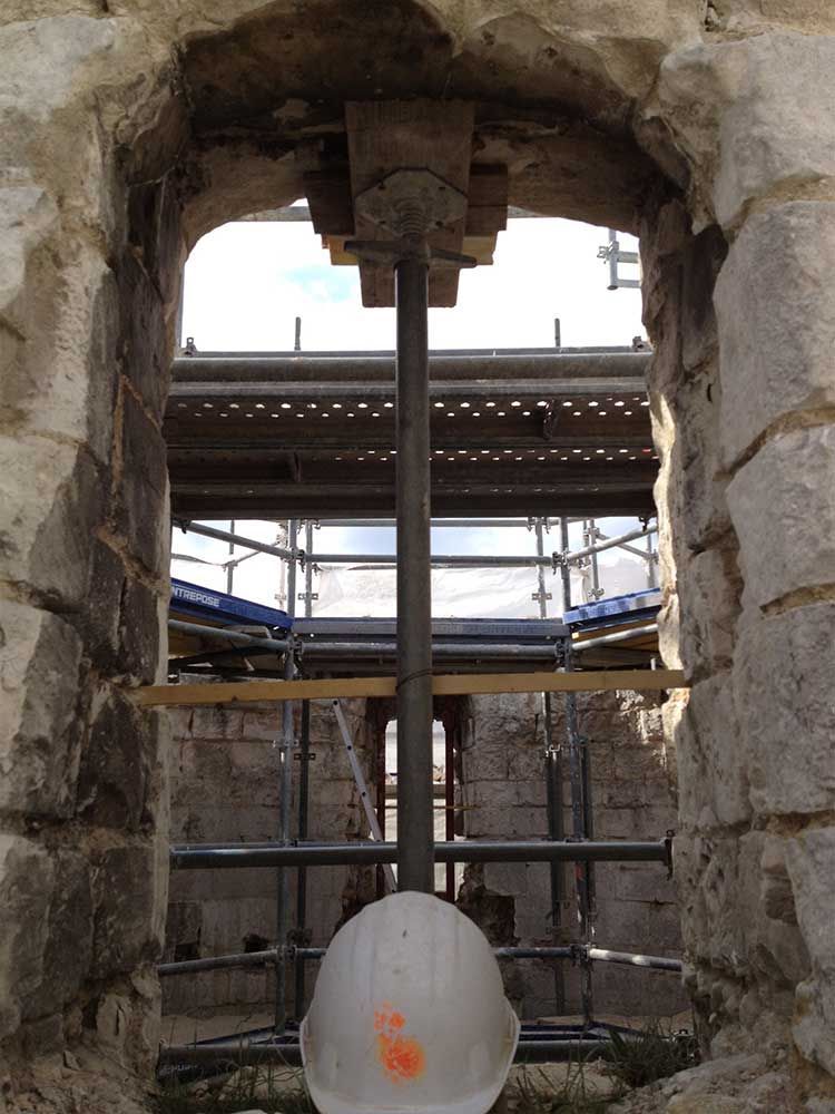 Fenêtre avec échafaudage et étai soutenant la structure ; un casque de chantier blanc est suspendu en dessous.