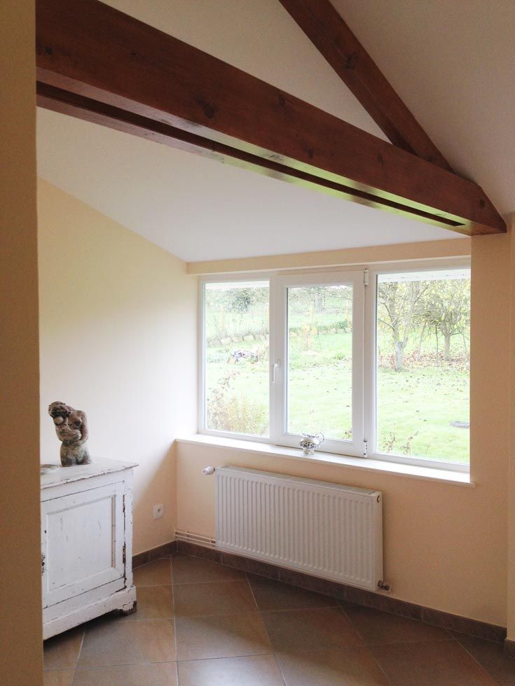 Coin intérieur avec fenêtre, meuble blanc, poutres brunes et radiateur.