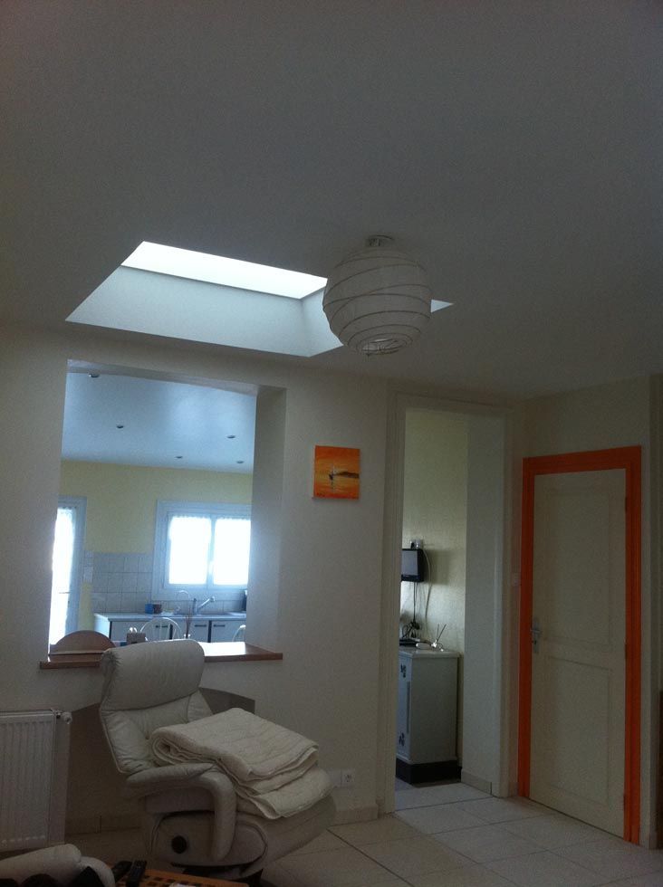 Vue intérieure d'un espace de vie avec puits de lumière, fauteuil inclinable et porte donnant sur la cuisine.