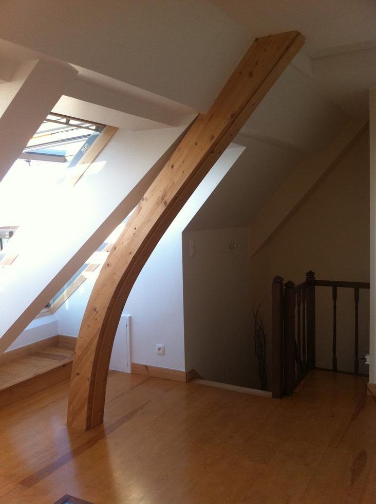 Poutre en bois cintrée traversant un grenier, soutenant la toiture.