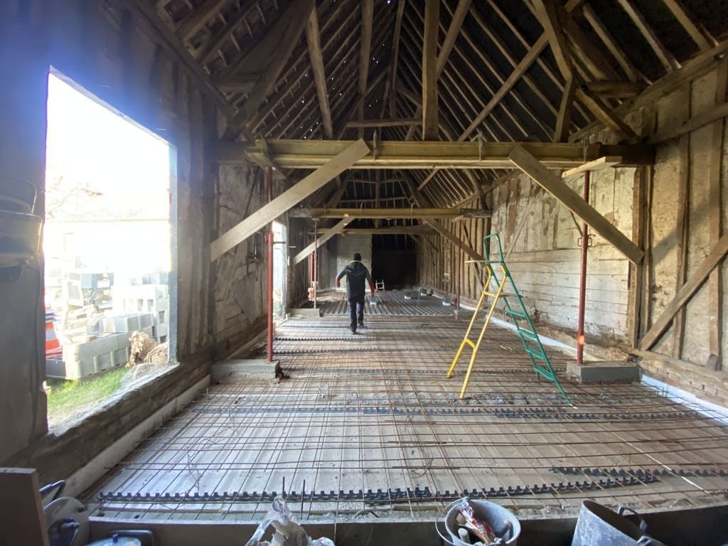 À l'intérieur d'une grange en construction ; une personne marche sur des barres d'armature ; poutres en bois, supports et fenêtre ouverte.
