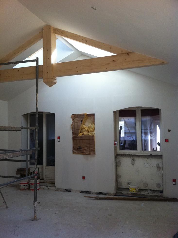 Intérieur d'une pièce en construction avec une poutre en bois, une fenêtre et un mur apparent.