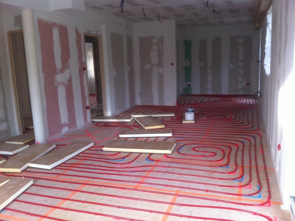 Pièce intérieure en construction, avec un système de chauffage au sol radiant rouge visible.