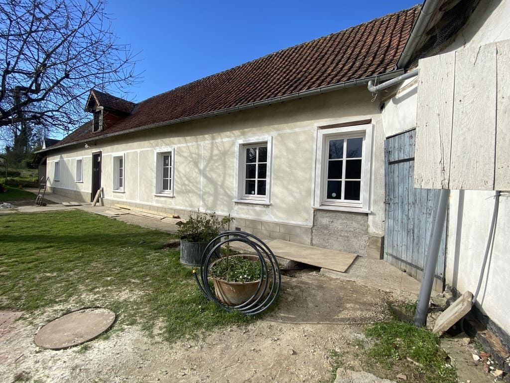 Un long bâtiment de plain-pied, avec un toit de tuiles rouges, des fenêtres à cadre blanc et une porte bleue, par une journée ensoleillée.