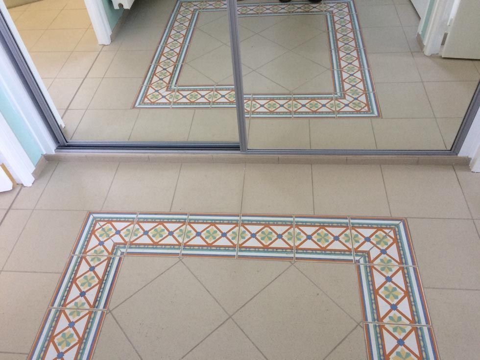 Le miroir reflète un sol carrelé beige orné d'une frise décorative.