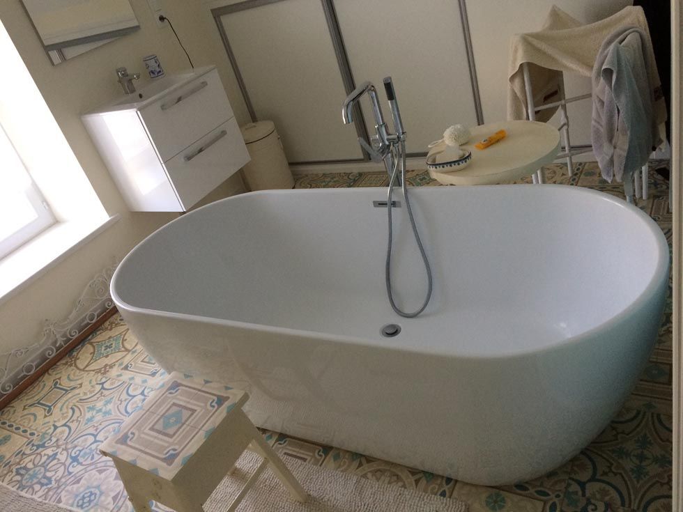 Baignoire ovale blanche dans une salle de bains avec carrelage à motifs au sol et un petit tabouret devant.