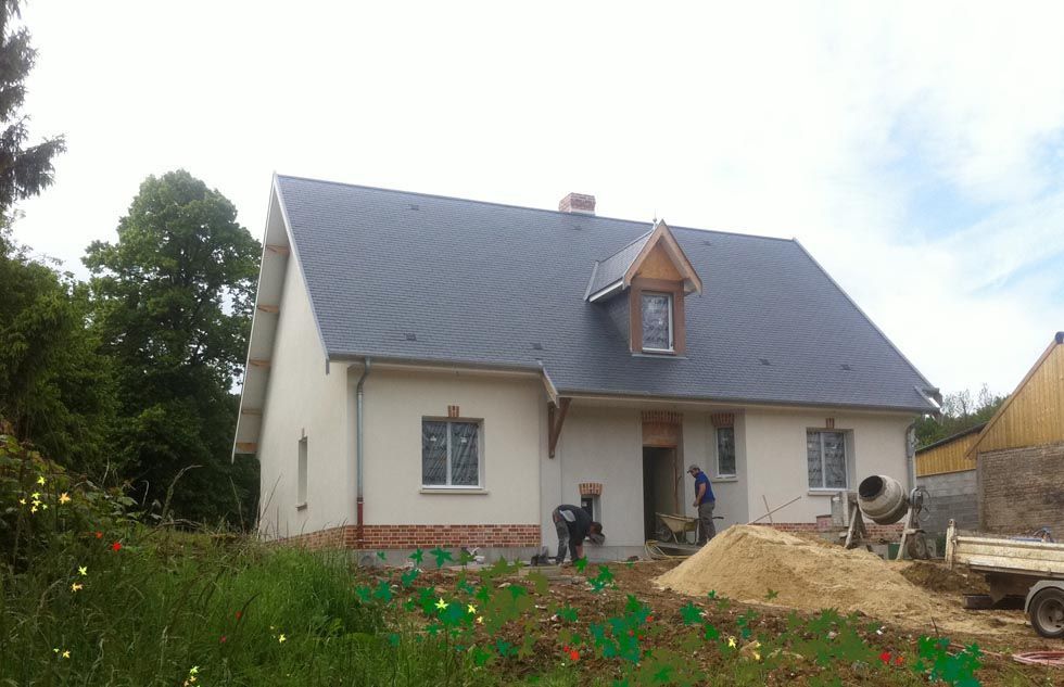 Maison en construction avec des ouvriers, du sable et une bétonnière à l'extérieur.