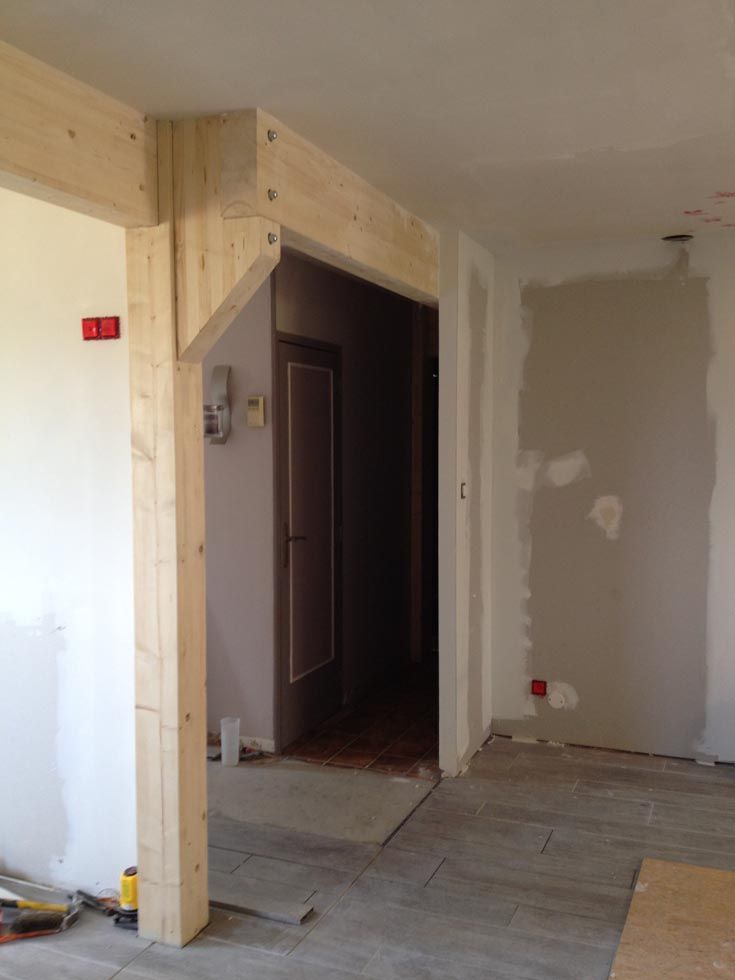 Cadre en bois d'une porte en construction. Poutres en bois beige, avec une porte donnant sur un couloir.