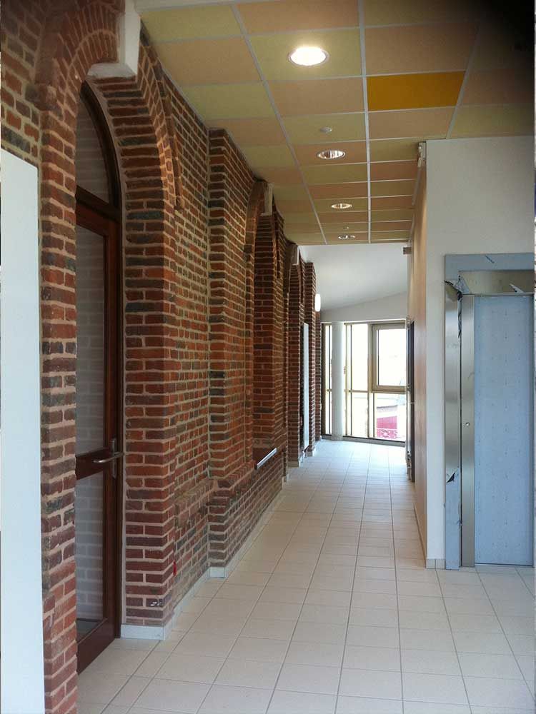 Couloir avec arches en briques et sol carrelé, menant à une porte lumineuse.