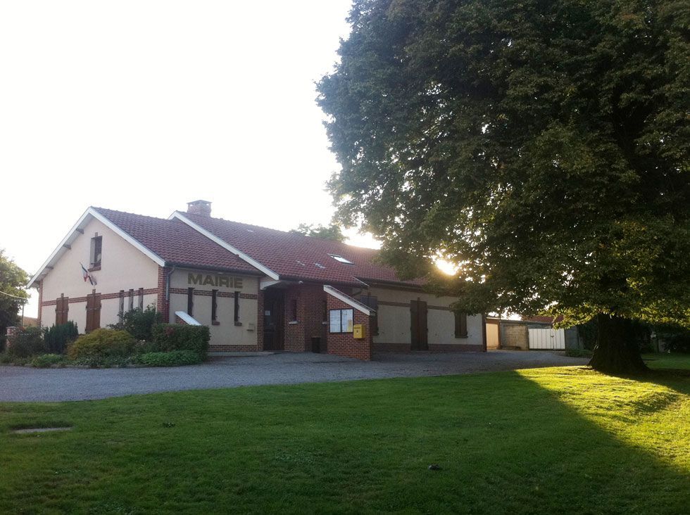 Un bâtiment en briques beiges et rouges portant l'inscription MAIRIE, avec une pelouse verte et un arbre par une journée ensoleillée.