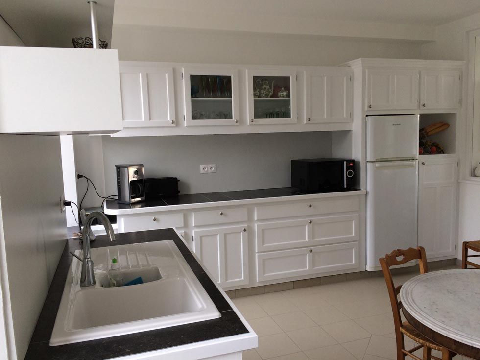 Cuisine blanche avec placards hauts et bas, plan de travail noir, évier et électroménager.