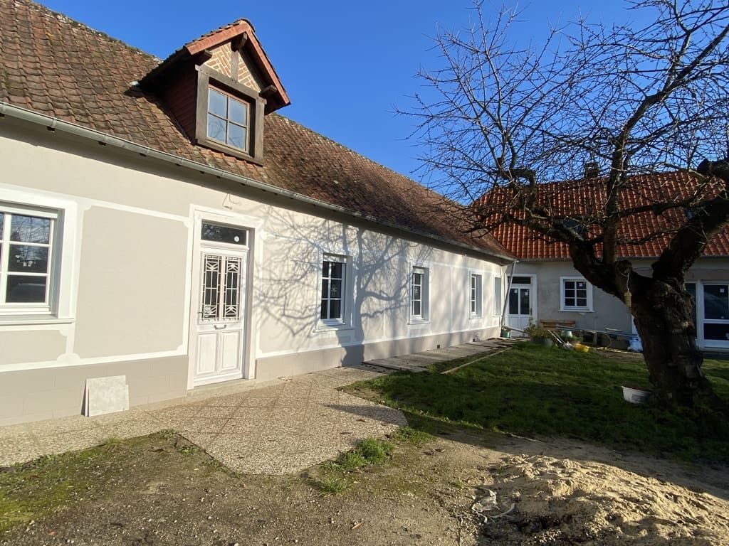 Une maison blanche au toit rouge, avec une lucarne et un chemin de gravier, par une journée ensoleillée.