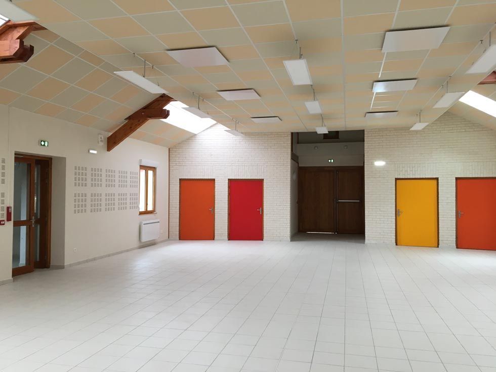 Hall lumineux et vide, avec sol carrelé blanc, portes colorées et éclairage au plafond.