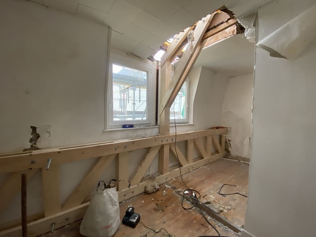 Pièce intérieure en construction, avec ossature bois, fenêtre, poutres apparentes et murs blancs.