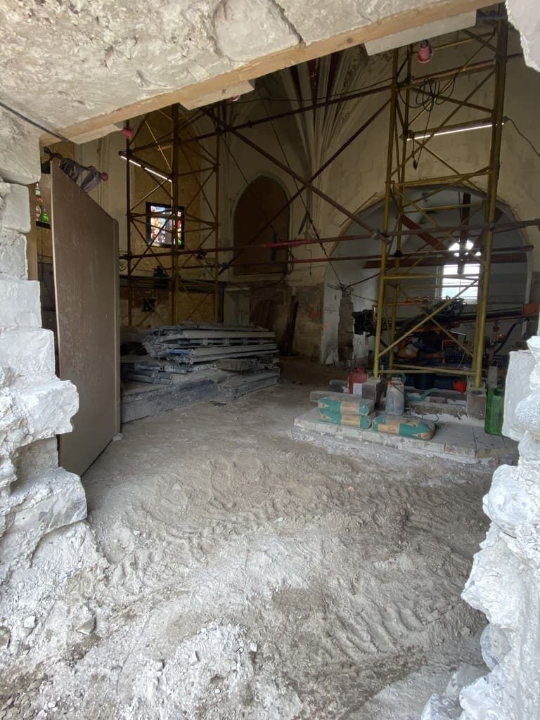Intérieur d'un bâtiment en construction, échafaudages visibles. Murs en pierre, plafond voûté et matériaux de construction sont présents.