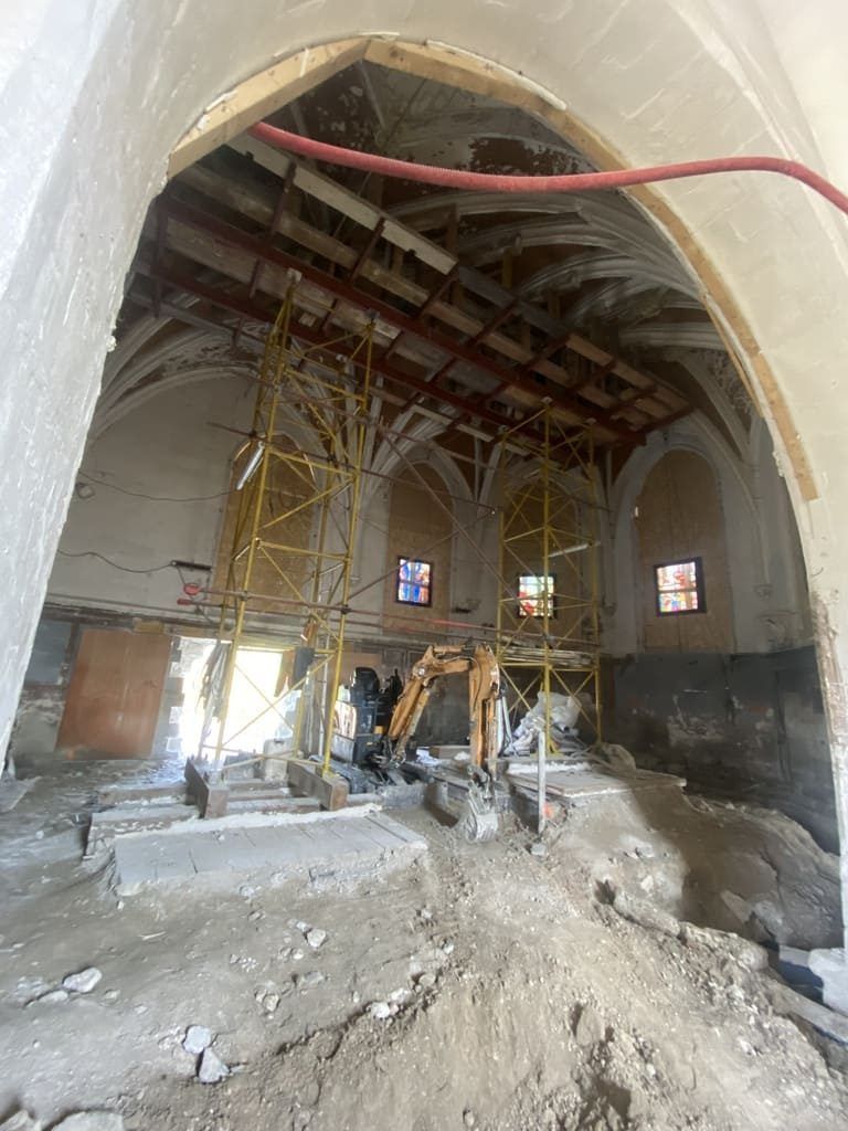 Intérieur d'un bâtiment en rénovation, avec échafaudages, engins de chantier et plafond apparent.