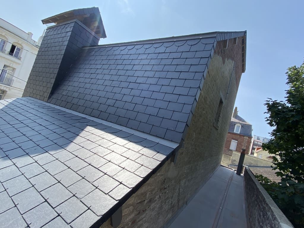 Toit d'ardoise sur un bâtiment en briques avec cheminée, sous un ciel bleu ensoleillé.