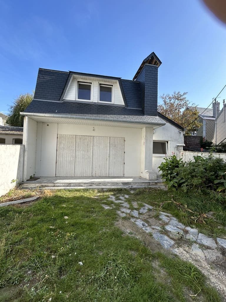Bâtiment blanc avec portes de garage, lucarnes et cheminée ; ciel bleu.
