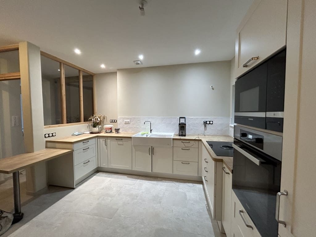 Cuisine moderne avec placards clairs, appareils électroménagers foncés et une petite table.