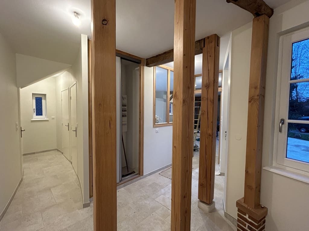 Couloir intérieur avec poutres apparentes, murs clairs et une fenêtre.