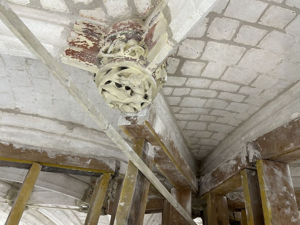 Plafond en plâtre orné et abîmé, avec des sculptures complexes et des poutres de soutien apparentes.