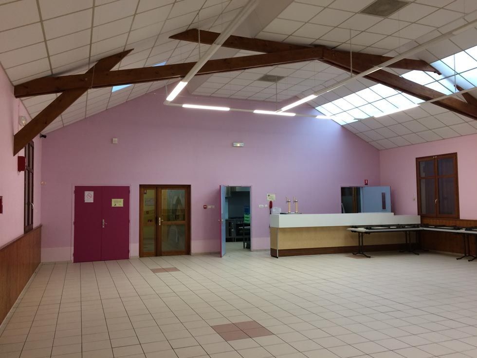 Hall vide aux murs roses, carrelé de carreaux clairs, avec poutres en bois, portes et comptoir. Des puits de lumière apportent de la lumière naturelle.