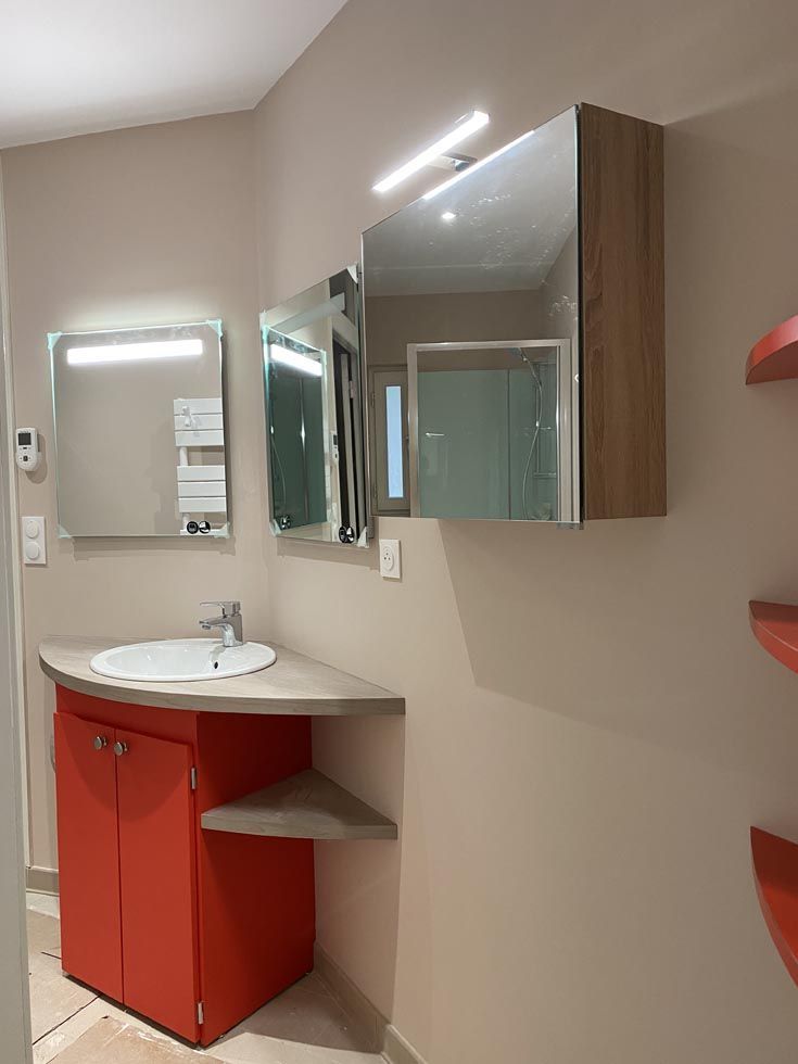 Une petite salle de bains avec un meuble-lavabo rouge, un lavabo rond et trois miroirs.