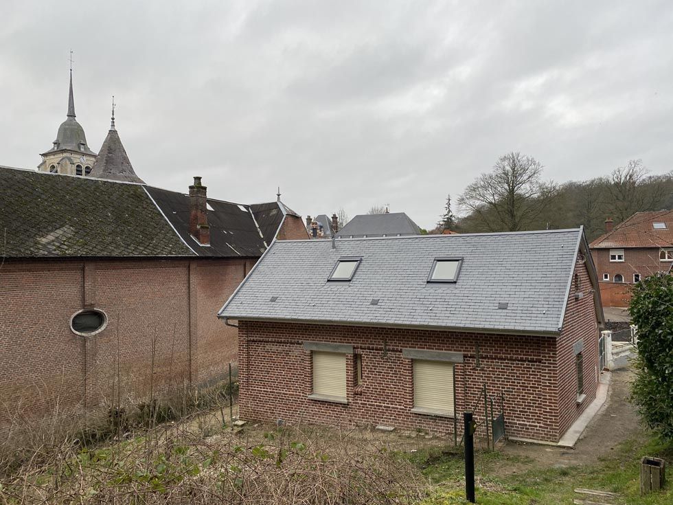 Bâtiment en briques avec deux puits de lumière devant une église à flèches par temps nuageux.