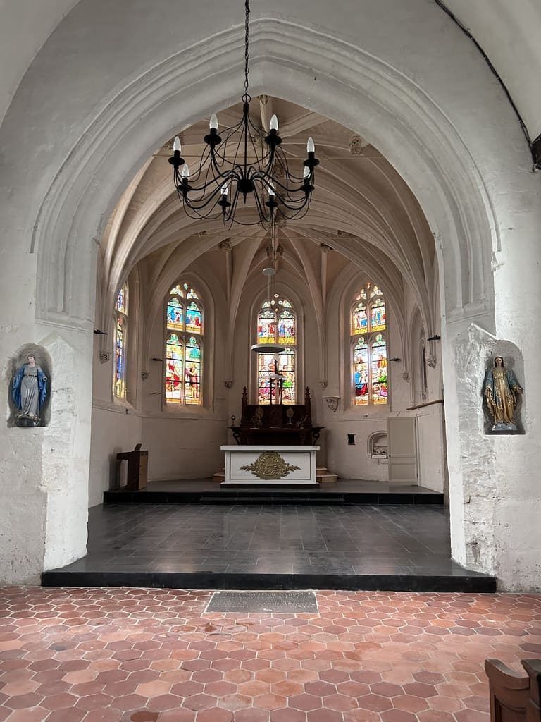 Intérieur d'une église avec plafond voûté, vitraux et lustre au-dessus de l'autel.